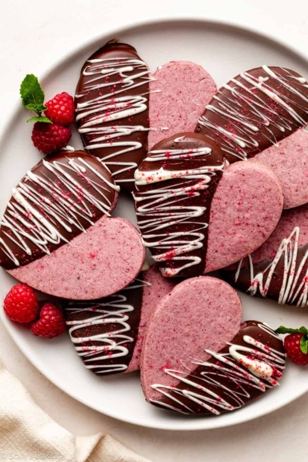 heart-shaped raspberry sugar cookies dipped in chocolate and white chocolate on white plate.